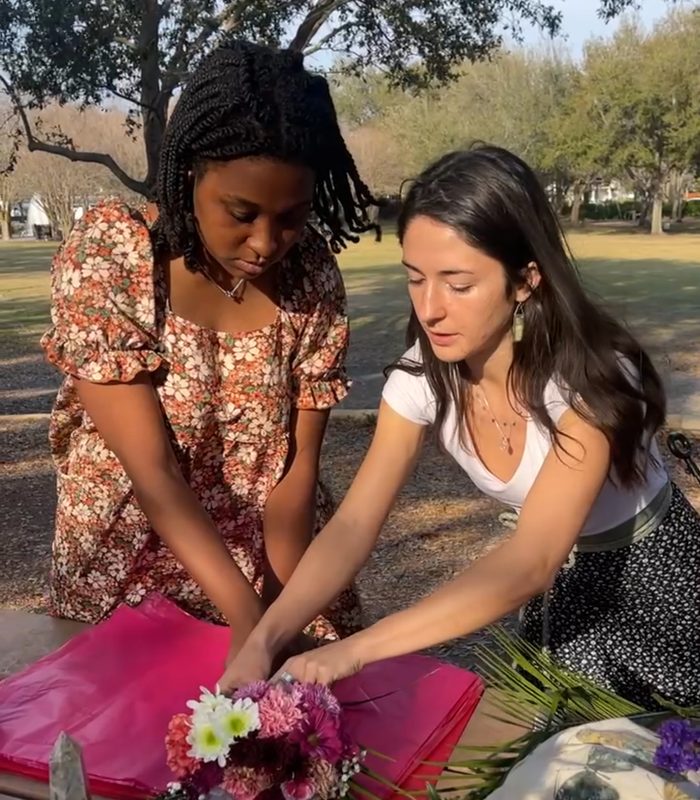 Two women wrapping a bouquet of flowers together in a park