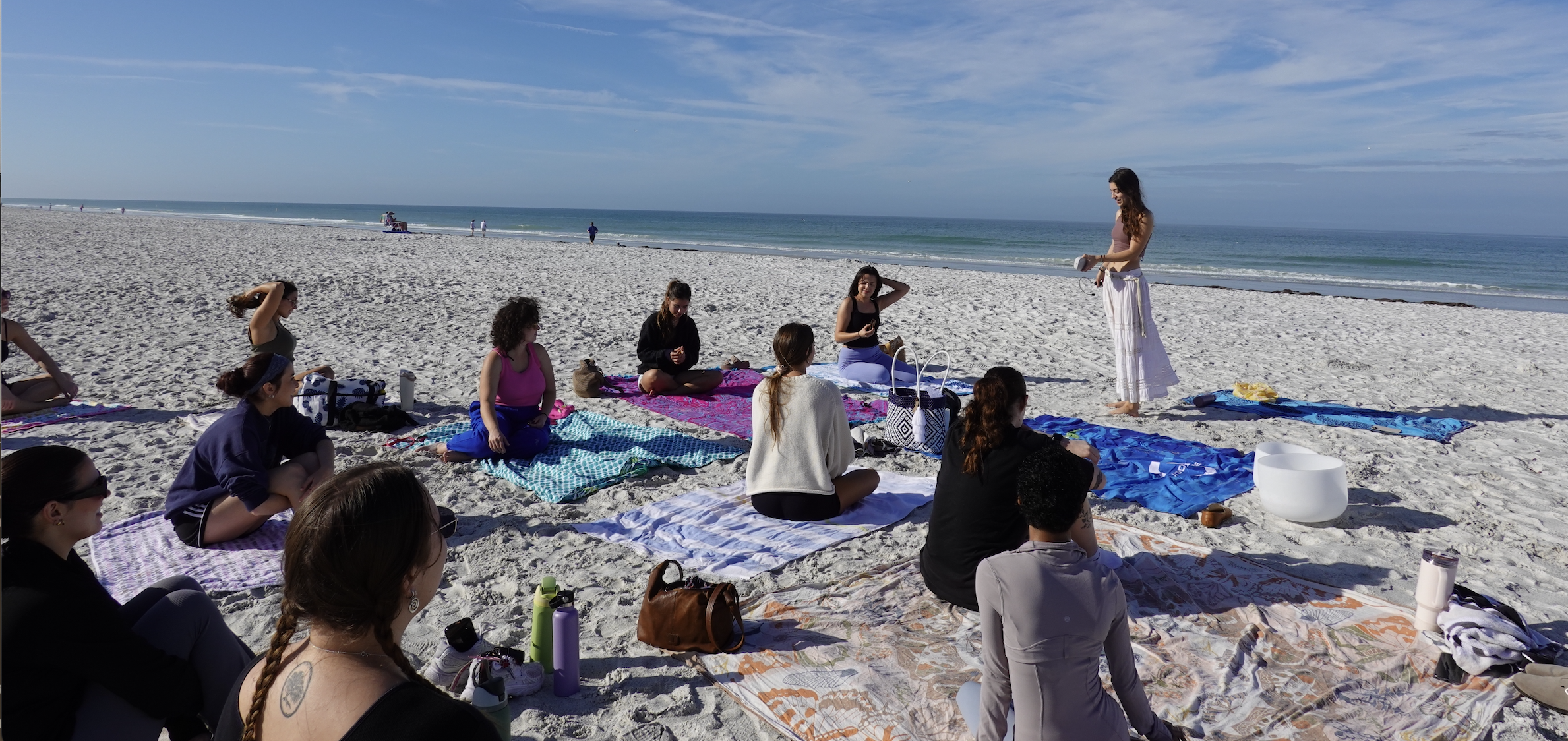 Bella Engelman leading a large beach yoga gathering in a white skirt