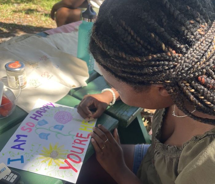A Mavens member hand-lettering a card that reads 'I am so happy you're here'