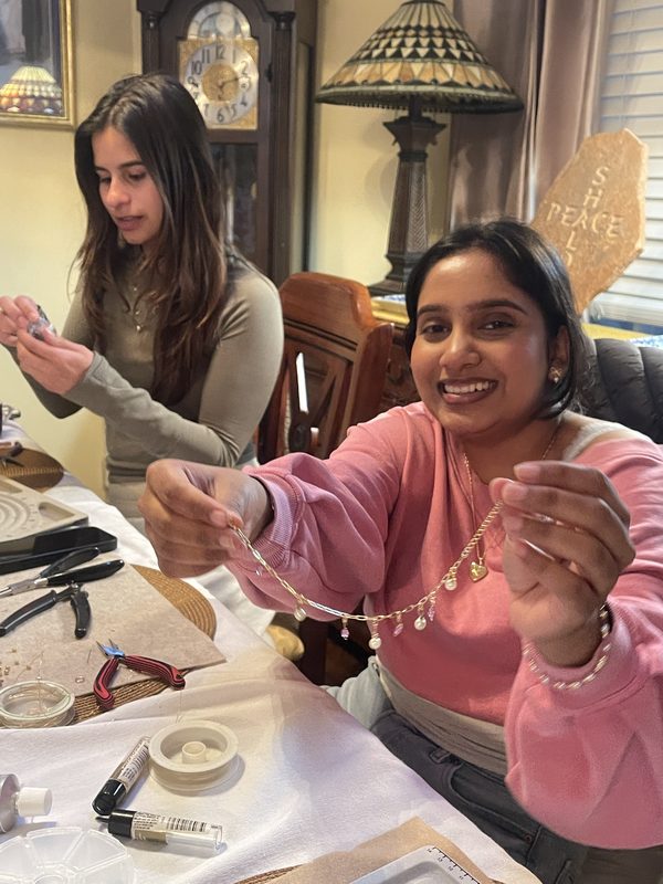 A Mavens member smiling and holding up handmade jewelry at a workshop